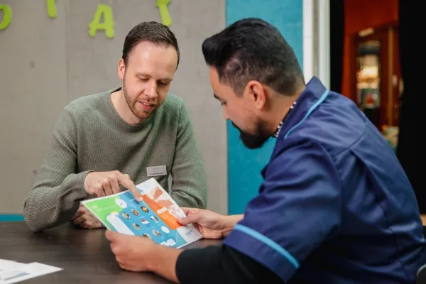 groepsbegeleider en medewerker zitten samen aan tafel terwijl er iets uitgelegd wordt